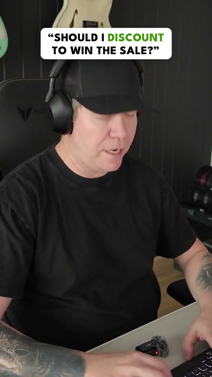 Paul Warren at the studio desk in a black cap and headphones, under the question card: Should I discount to win the sale?